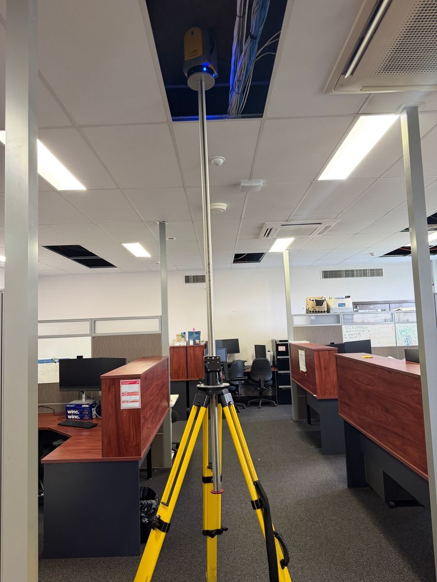 Laser scanner on an elevating tripod raised through an open ceiling tile in an office